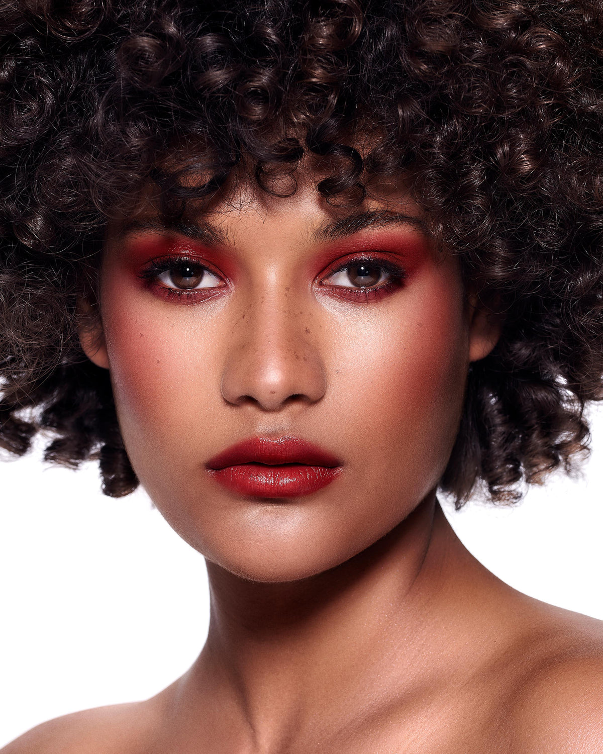 Close-up of a model with medium-deep skin wearing red lip and cheek makeup